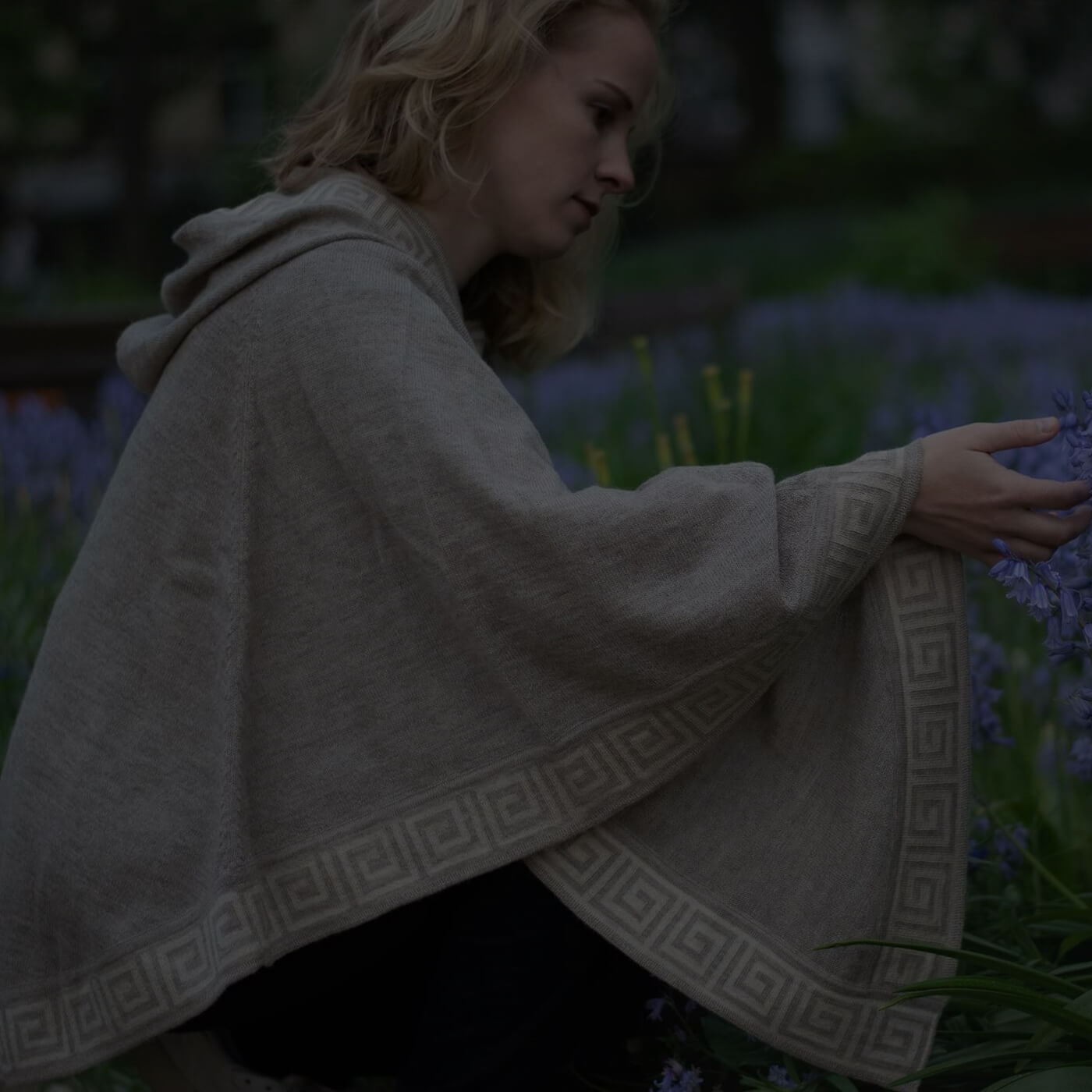 Blonde Frau trägt Luz Alpaka Poncho von Alpakin in beige und berührt eine Blume