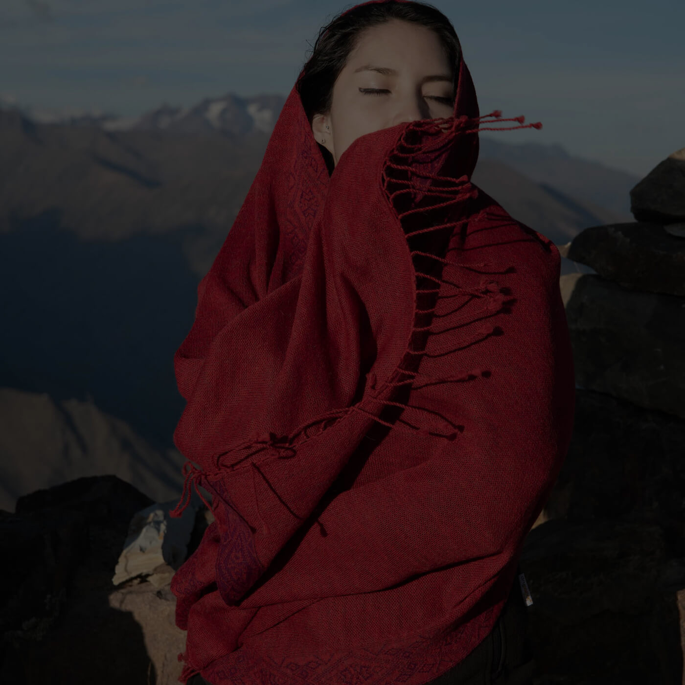Frau vor Bergkulisse hüllt sich in den roten Flor Alpaka Poncho Schal von Alpakin - weich aus 100% Babyalpaka, ohne Kunstfasern.