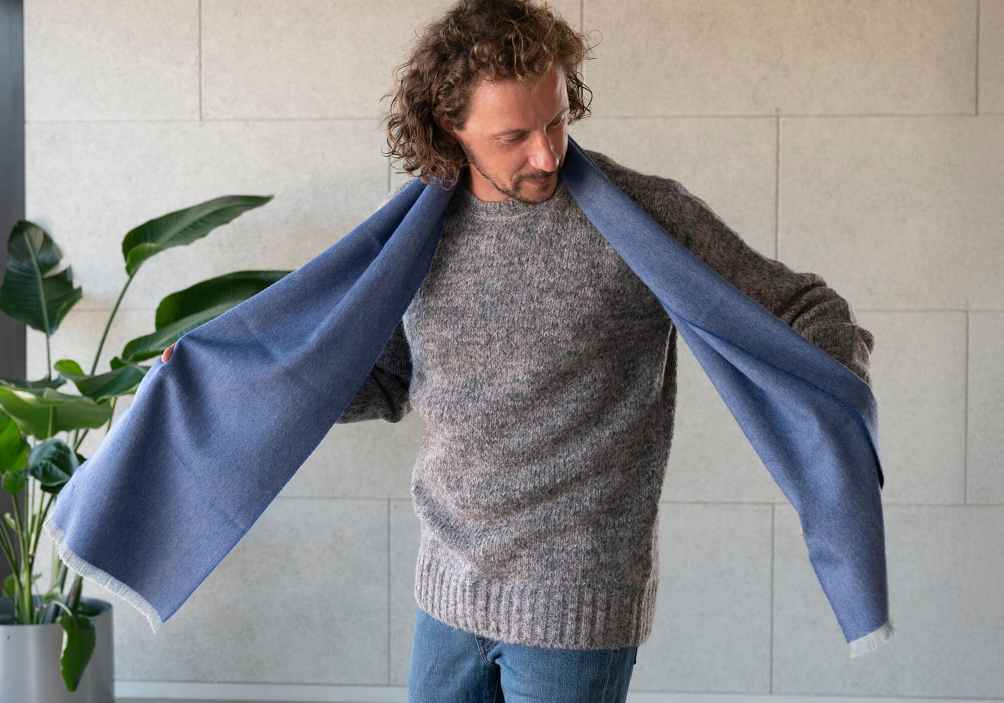 Mann trägt den Chikan Alpaka Pullover in grau von Alpakin und kombiniert diesen mit dem weichen Premium Babyalpaka Schal in blau
