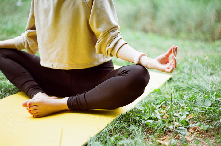 Frau sitzt auf Yoga-Matte im Grünen und praktiziert Yoga