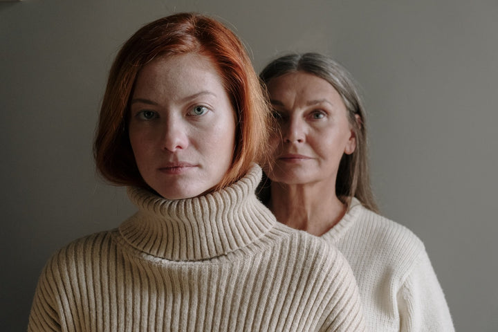 Zwei Frauen mit Wollpullover die hintereinander stehen und ernst in die Kamera blicken