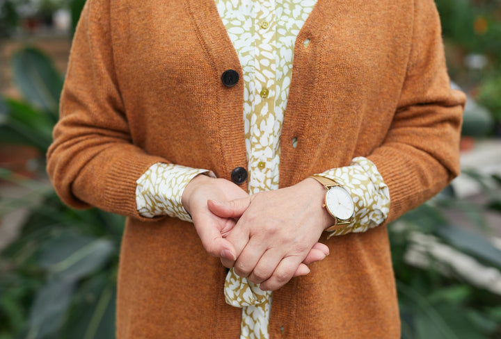 Frau trägt edle, orangene Alpaka Strickjacke mit gemusterter Bluse