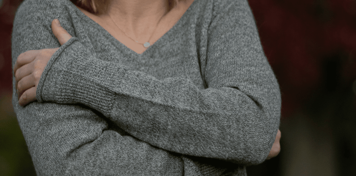 Alpaka Pullover Damen von Alpakin in hellgrau mit V-Ausschnitt getragen von einer Frau, die sich umarmt