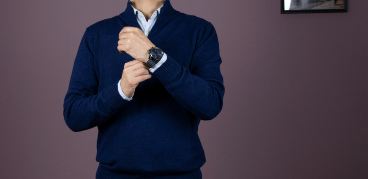 Dunkelblauer Alpaka Pullover und Hemd getragen von einem Mann, der sich an die Uhr fasst