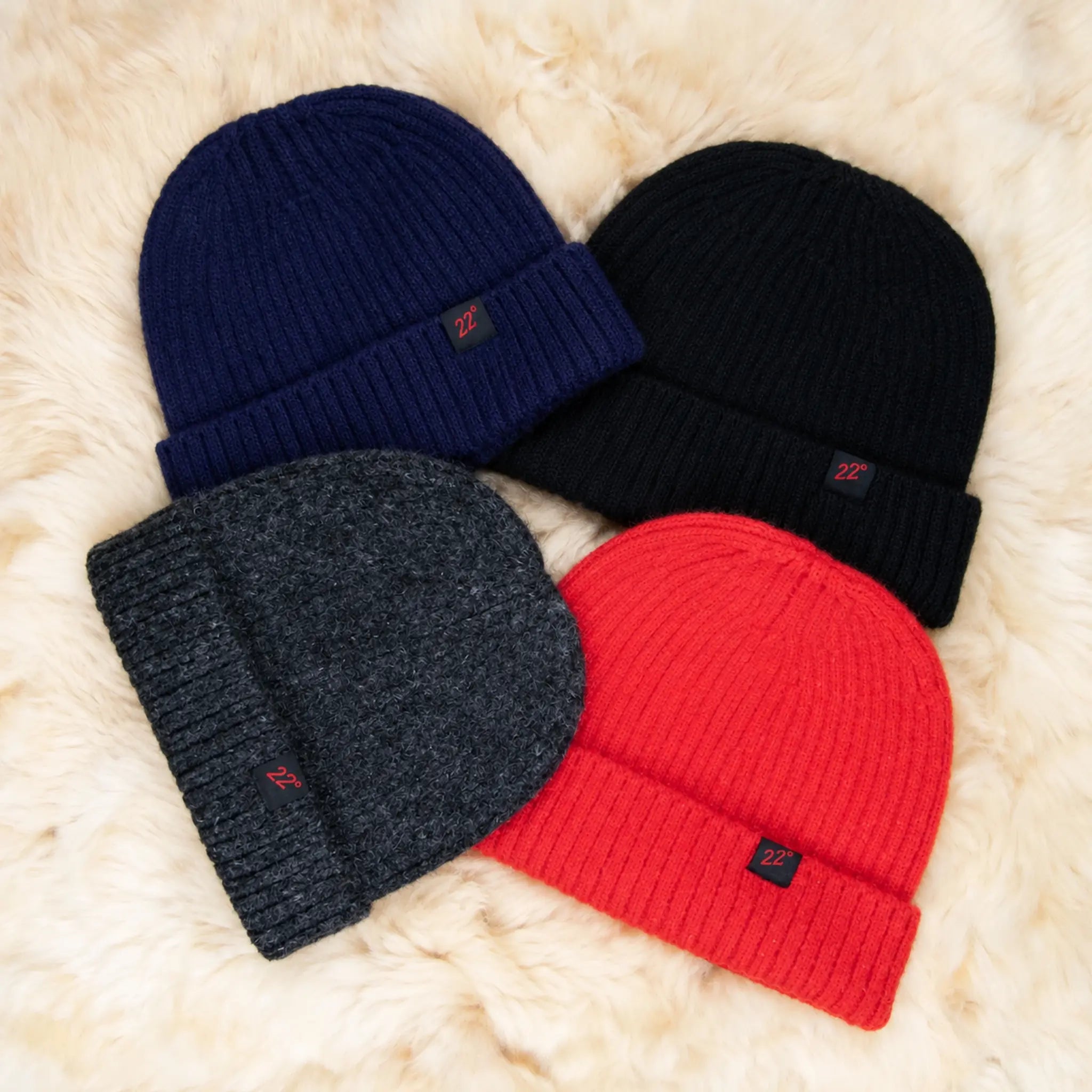 Winddichte Alpaka Beanie in den vier Farben schwarz, dunkelblau, Holzkohle und rot liegen auf einem weichen Alpaka Fell