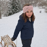 Mädchen trägt mein Schlittenfahren warmes Stirnband mit Knoten aus Alpakawolle in ihrer Lieblingsfarbe rosa