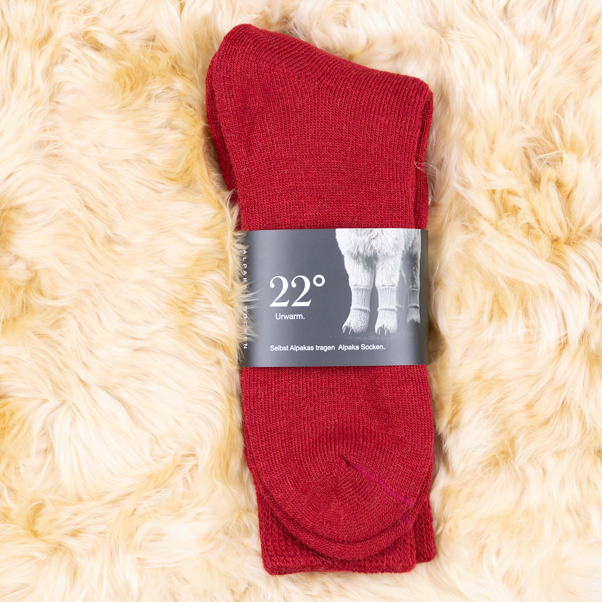 Alpaka Wintersocken in rot, verpackt und liegend auf weichem Alpakafell