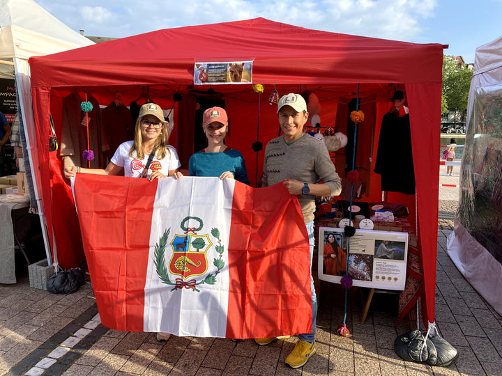 Alpakin Gründer mit peruanischer Flagge vor ihrem Stand für Alpaka Kleidung aus Peru am lateinamerikanischen Wochenende in Köln 2023