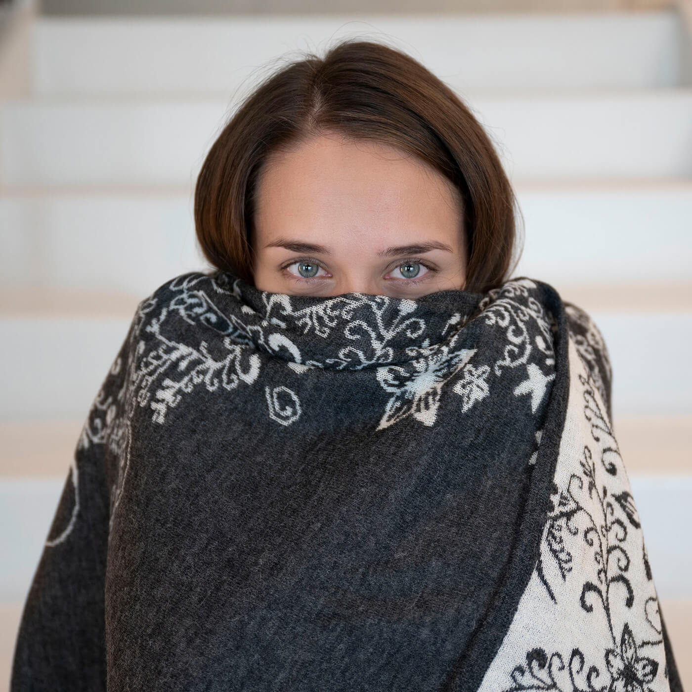 Frau kuschelt sich in den sanften Alpaka Wendeponcho in Holzkohle mit Blumenmuster
