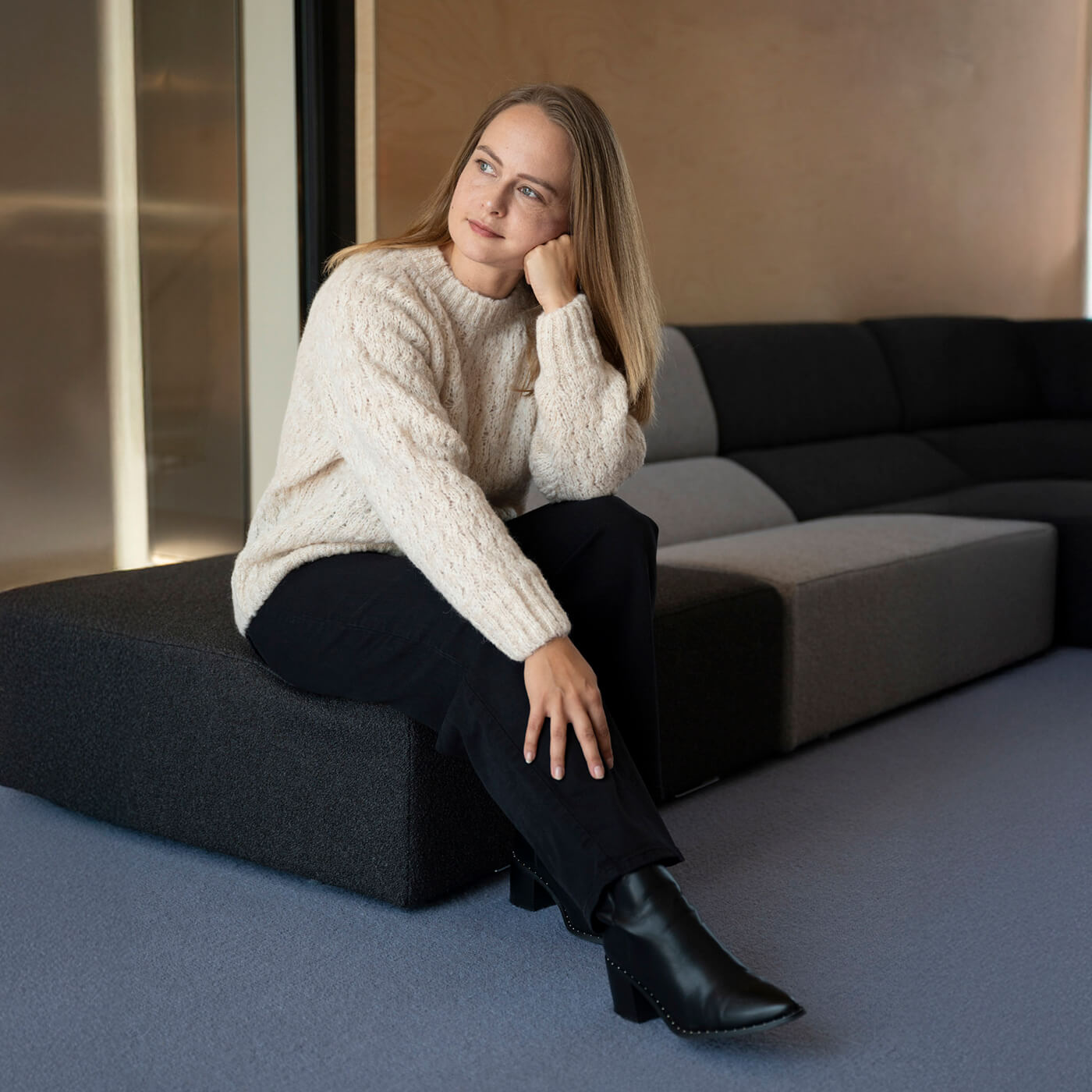 Sitzende Frau legt ihren Kopf auf ihre Faust und trägt den kuschelweichen Liya Alpaka Strickpullover in Naturfarbe creme