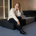 Sitzende Frau legt ihren Kopf auf ihre Faust und trägt den kuschelweichen Liya Alpaka Strickpullover in Naturfarbe creme