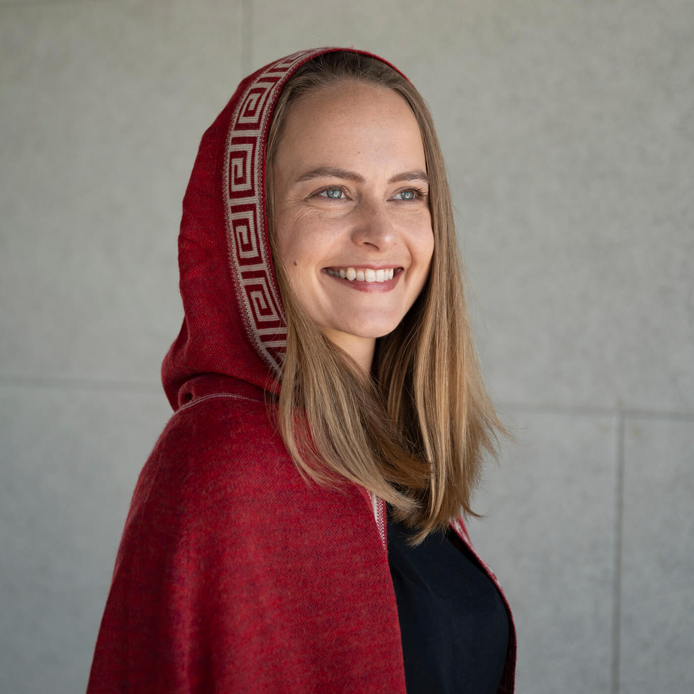 Lächelnde Frau trägt den Luz Alpaka Poncho in rot von Alpakin mit Kapuze
