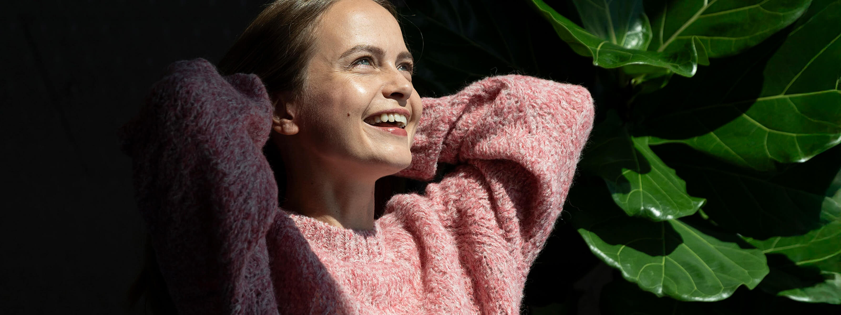 Frau mit rosafarbigem Liya Alpaka Strickpullover lacht glücklich der Sonne entgegen