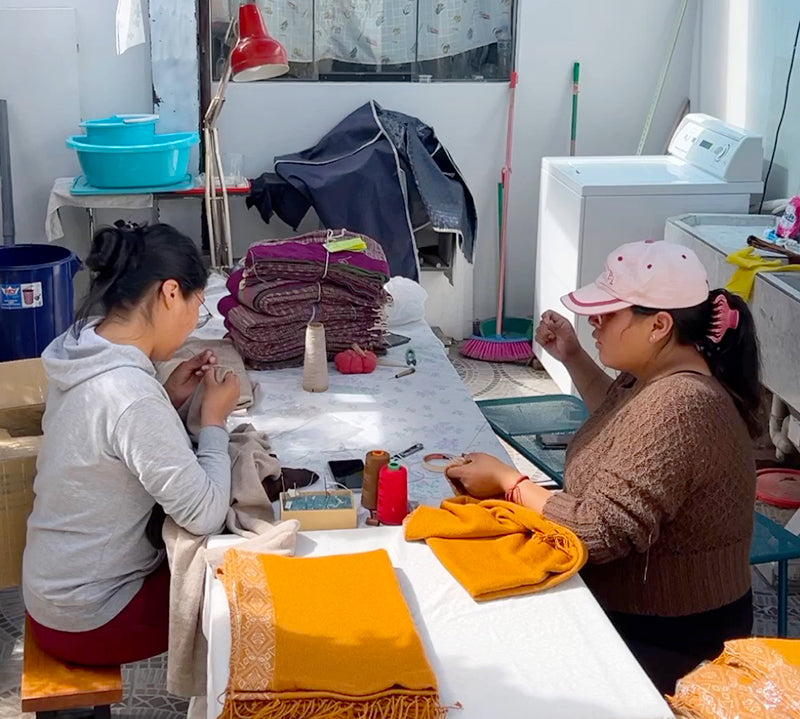 Fertigung Alpaka Poncho FLOR von Frauen in Peru, die am Tisch sitzen und arbeiten