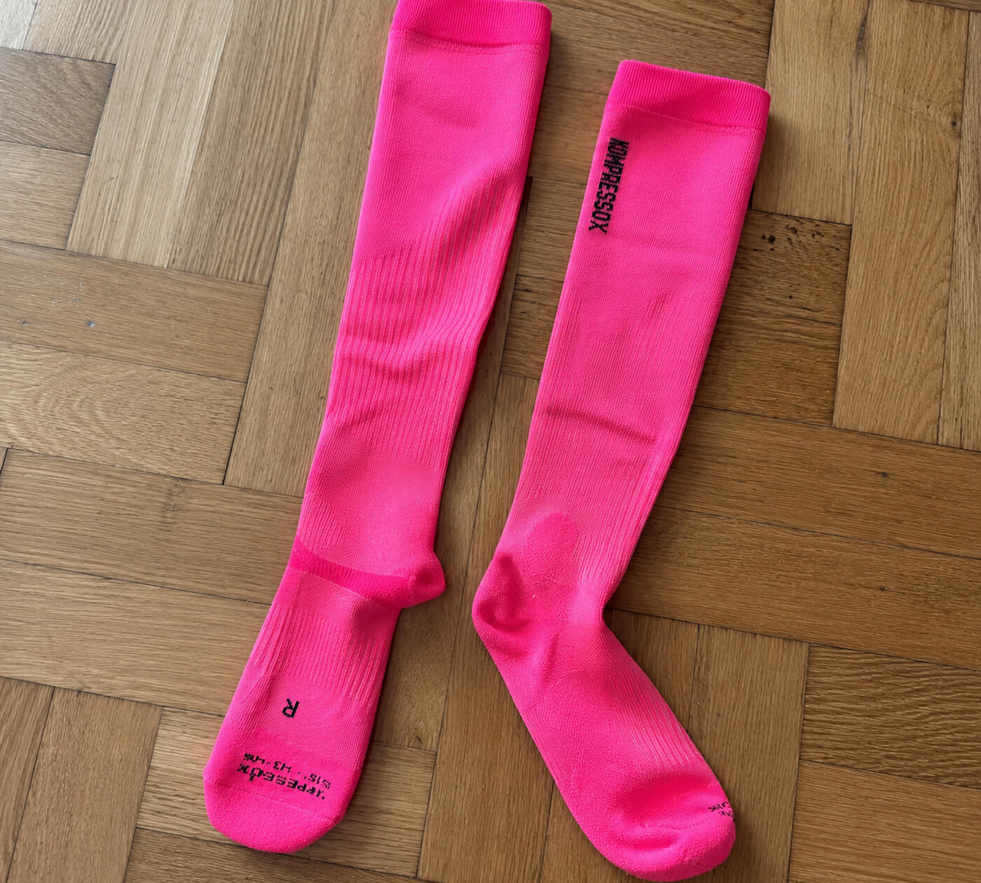 Pinke Kompressionsstrümpfe von Alpakin auf dem Holzboden liegend