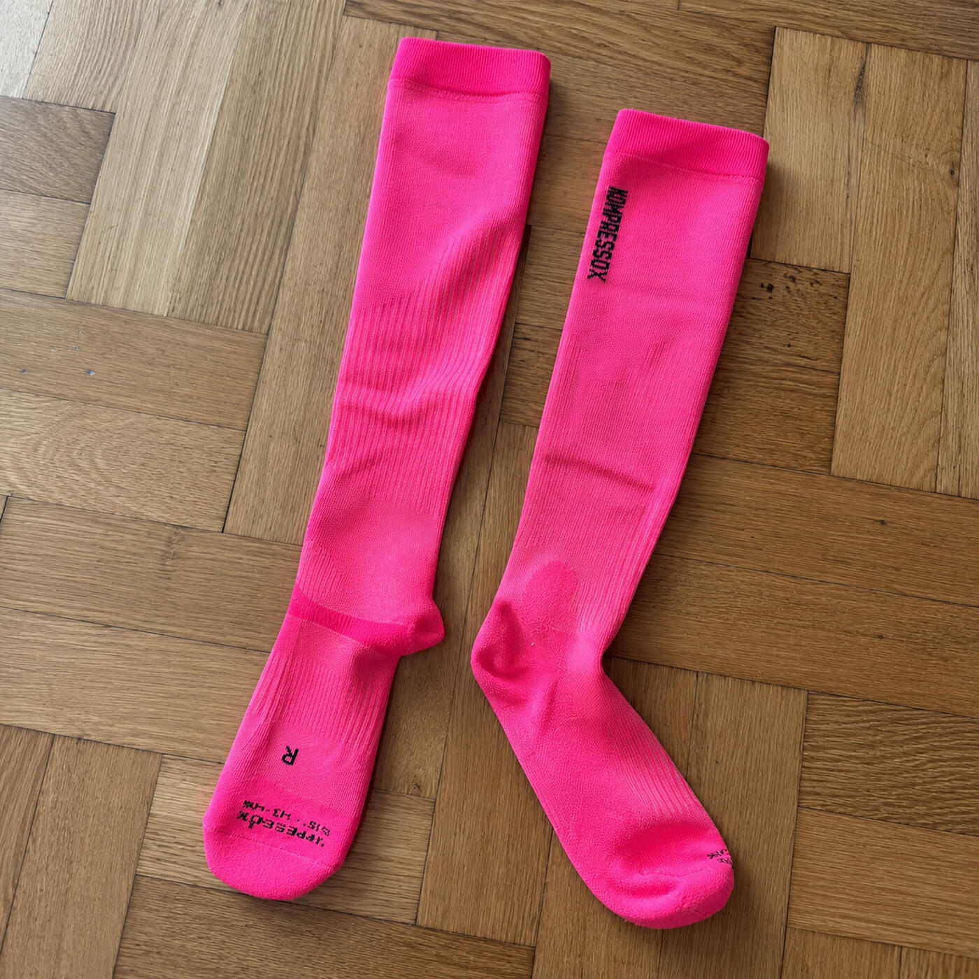 Pinke Kompressionsstrümpfe von Alpakin auf dem Holzboden liegend