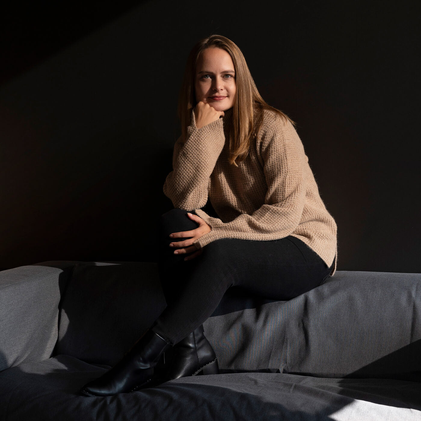 Frau auf schwarzem Sofa mit Alpaka Pullover in Naturfarbe hellbraun legt das Kind auf ihre Hand