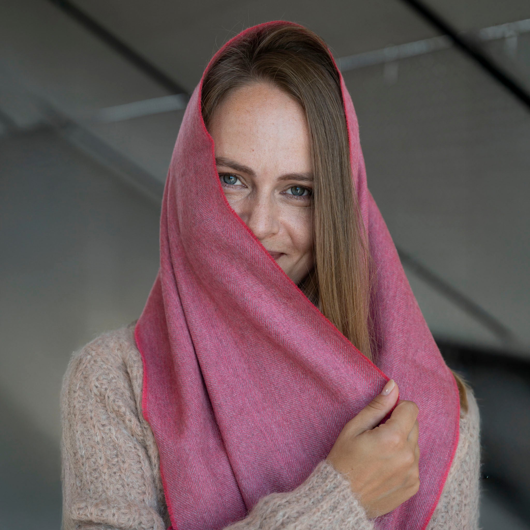 Frau bedeckt ihren Kopf mit dem Premium Babyalpaka Schal in pink mit Fischgrätenmuster