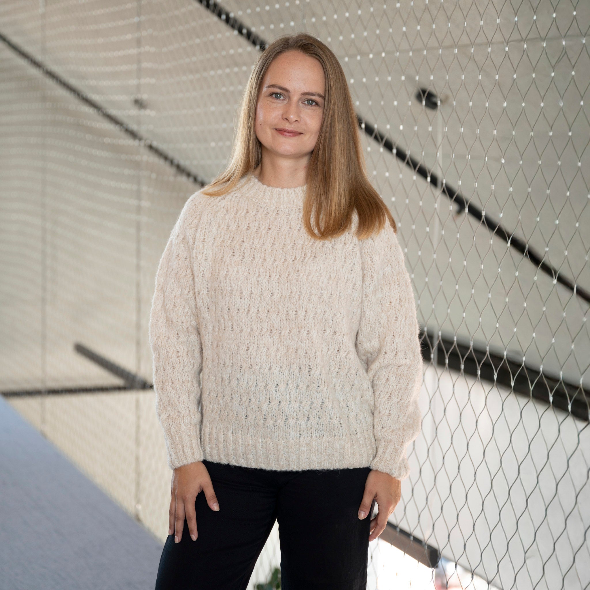 Frau trägt den Liya Alpaka Pullover von Alpakin in creme und blickt lächelnd in die Kamera