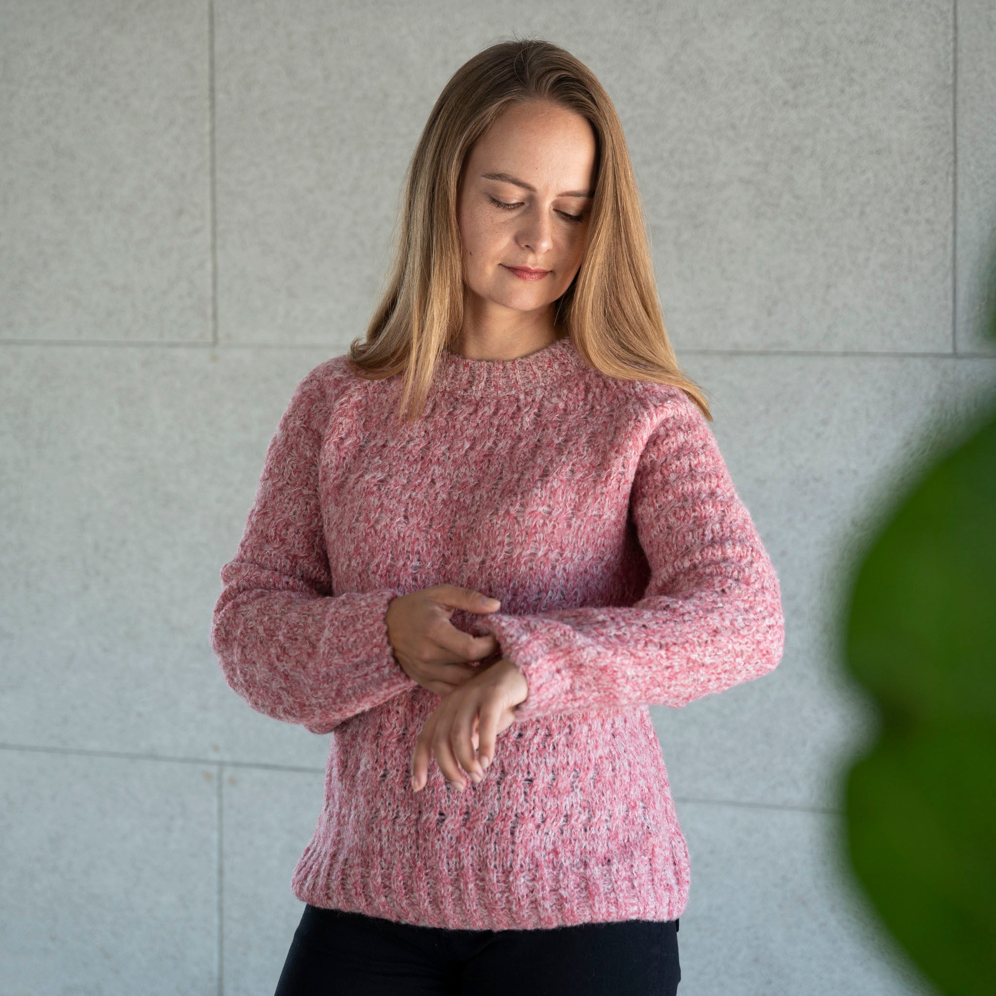 Blonde Frau trägt den Liya Alpaka Strickpullover von Alpakin in rosa und richtet sich den Ärmel