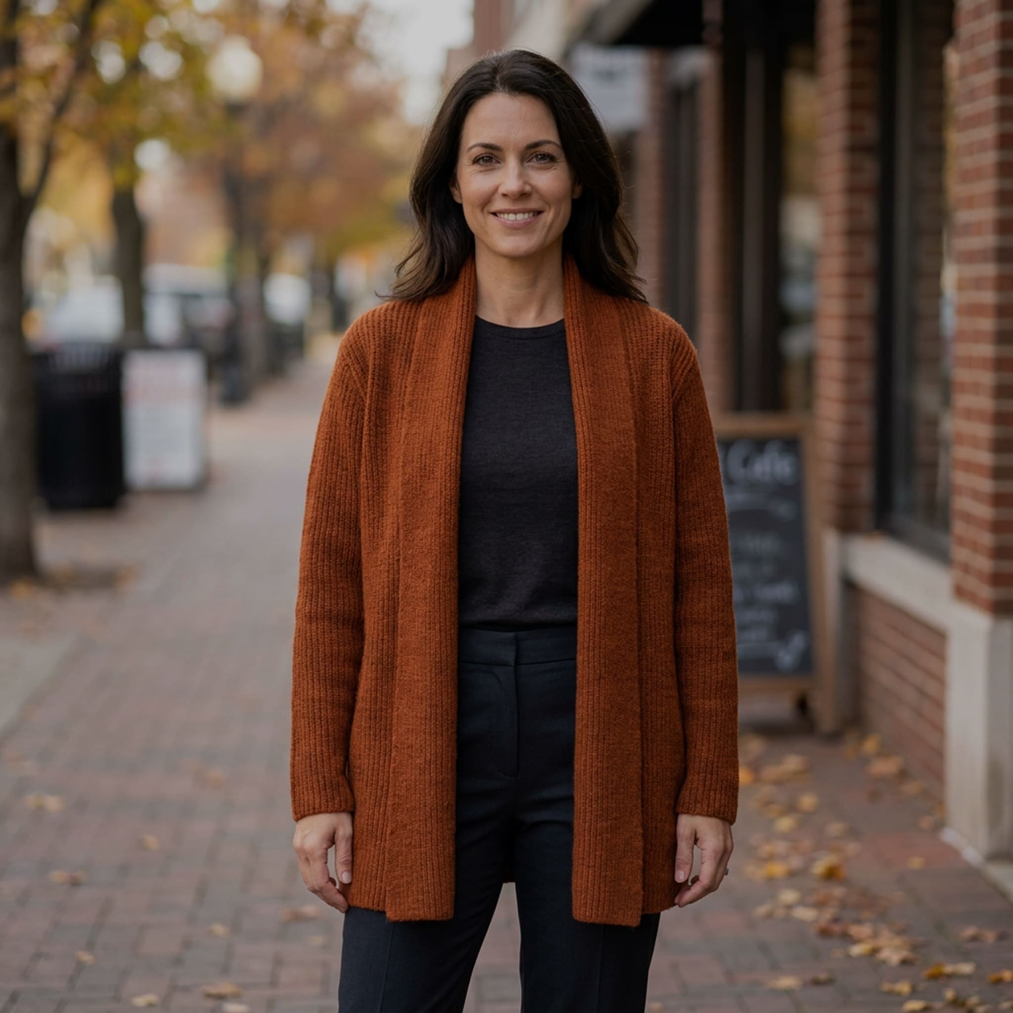 Frau trägt den warmen Alpaka Cardigan in stylischem dunkelorange vor herbstlicher Kulisse einer Stadt
