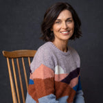 Selbstbewusste Frau blickt lächelnd in die Kamera und trägt den weichen Sumaq Alpaka Pullover in bunten Farben