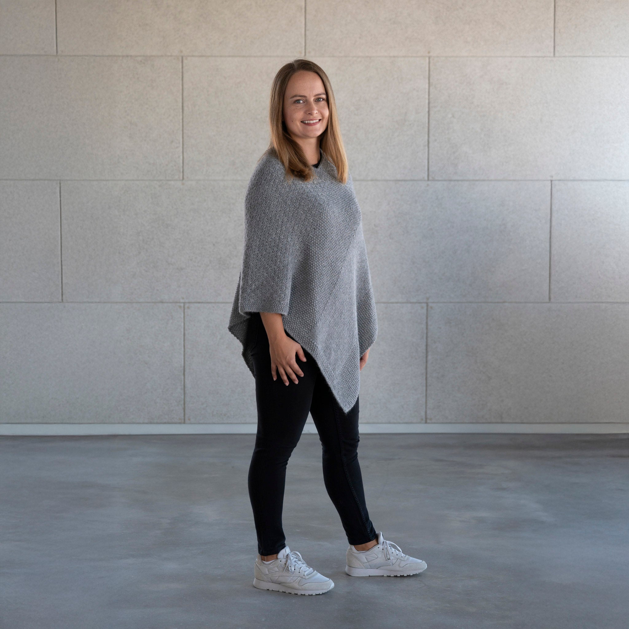 Frau trägt den Babyalpaka Strickponcho Naira in grau, gefertigt in der kleinen Alpakin Manufaktur in Peru