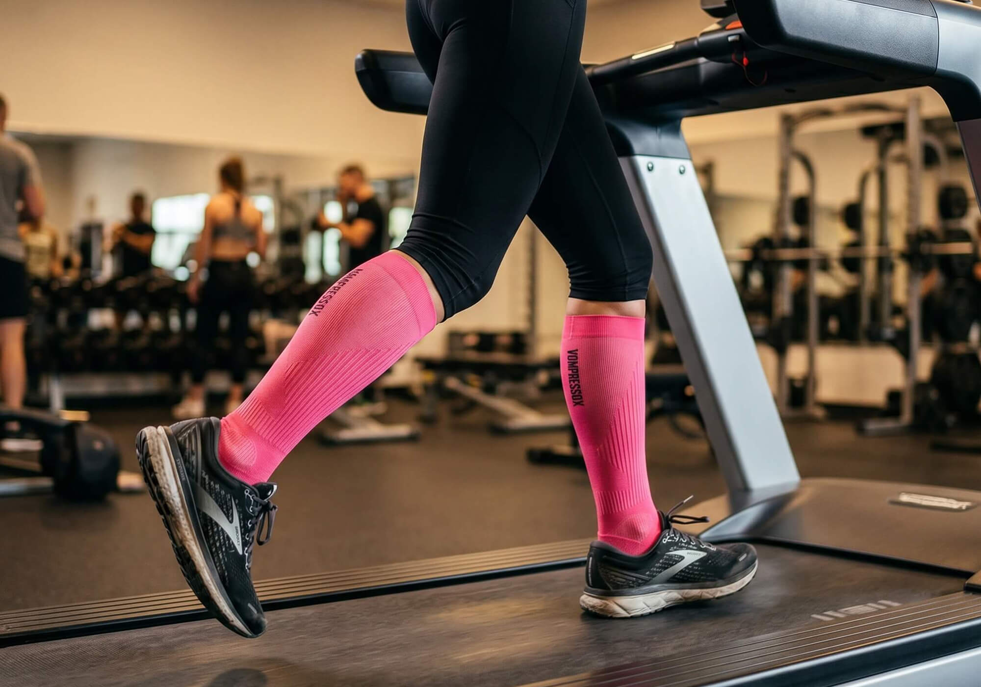 Frau trägt pinke Kompressionsstrümpfe auf dem Laufband im Fitness Studio