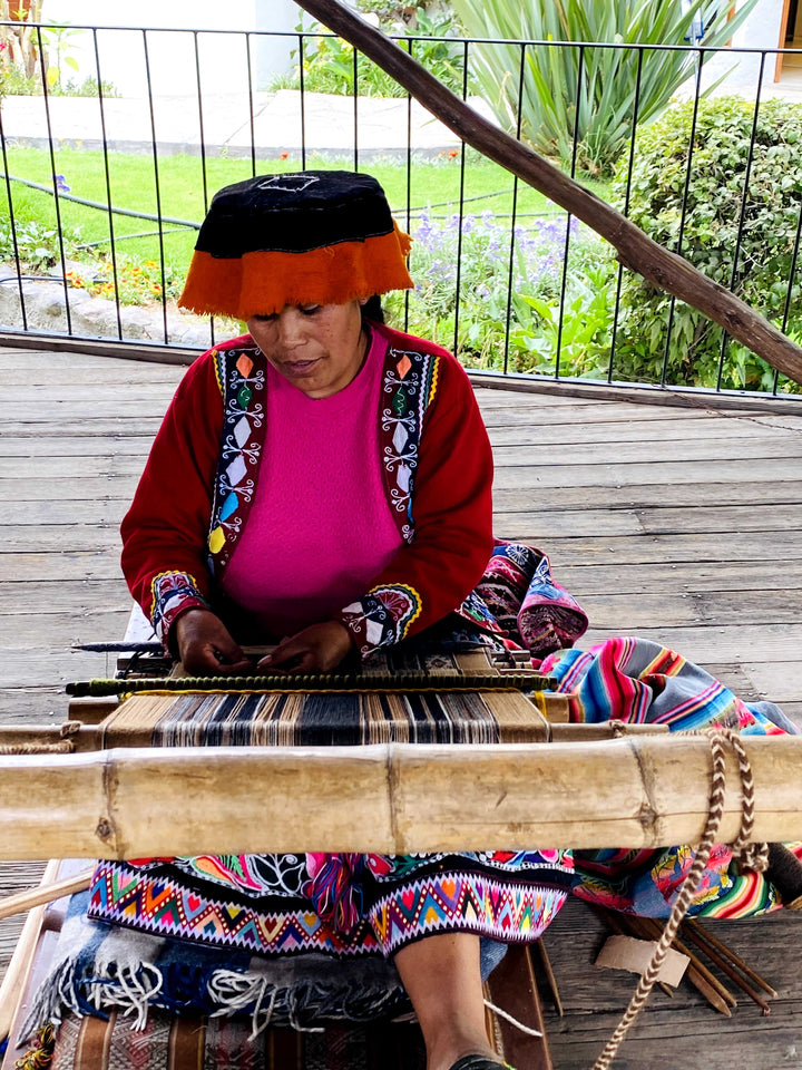 Peruanerin in typischer, bunter Kleidung webt mit Alpakawolle