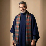 Ein attraktiver 45-järiger Mann mit Bart und grauen Haaren trägt den Herren Poncho mit Kragen British-Style - in Kombination mit dunkelrotem Schottenkaro Schal